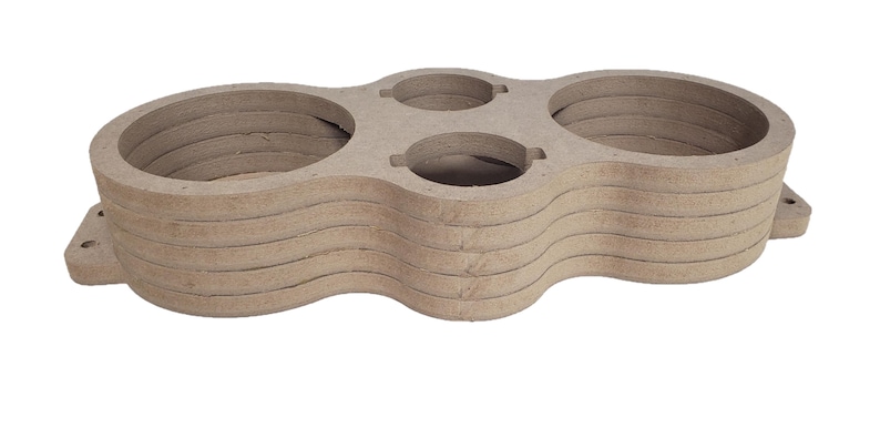 May include: A stack of unfinished MDF wood speaker enclosures. The enclosures have a light brown color and a layered design with circular and oval cutouts. The design includes mounting tabs on the sides.