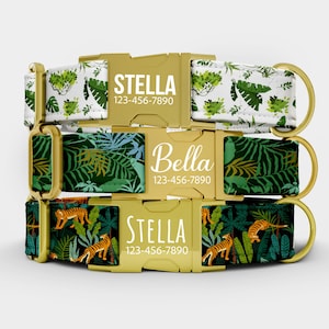 May include: Three dog collars with gold-colored buckles and rings. The collars feature jungle-themed patterns with green leaves, tigers, and the names "Stella" and "Bella" printed in white, along with a phone number.