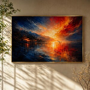 May include: A framed landscape painting depicts a vibrant sunset over a body of water. The sky transitions from deep blue to fiery orange and red, reflecting on the water's surface. A silhouette of a bird flies across the scene.