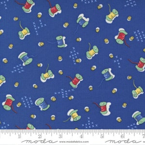 May include: Blue fabric with a repeating pattern of spools of thread in red, yellow, and blue, and small yellow buttons. The fabric has a white ruler with the word "moda" printed on it.