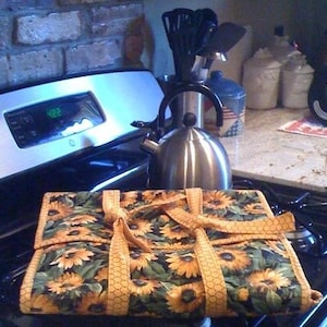 May include: A floral patterned fabric bread basket with a silver teapot and a set of utensils in the background.