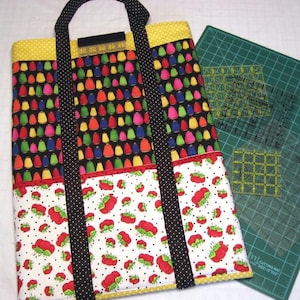 May include: A black and yellow tote bag with a black and white polka dot pattern. The bag has three pockets and is made of fabric. The bag is sitting on a green cutting mat with a ruler.