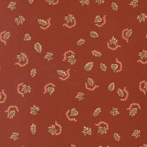 May include: A rust-coloured fabric featuring a repeating pattern of small, light-coloured leaves and delicate, curved vine-like sprigs scattered across the surface. The design consists of various leaf shapes in a soft, muted cream tone.