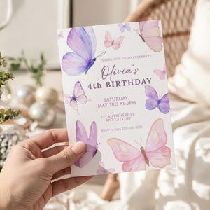 May include: A white invitation card featuring watercolor butterflies in shades of pink and purple. The text reads "Olivia's 4th Birthday" with event details. The card is held by a hand.