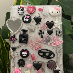 May include: A clear phone case adorned with a variety of charms, including hearts, stars, and a Hello Kitty figure. The case features the word "Barbie" and the text "I ♥ ME". The charms are in black, pink, and silver.