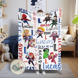 Puede incluir: Manta blanca con superh&eacute;roes de dibujos animados y el nombre "Lucas" en rojo y azul. La manta tiene un patr&oacute;n repetido del nombre y la letra "L" en una fuente l&uacute;dica, con varias ilustraciones de superh&eacute;roes.