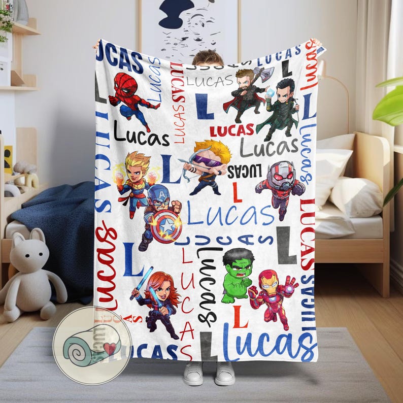 Puede incluir: Manta blanca con superh&eacute;roes de dibujos animados y el nombre "Lucas" en rojo y azul. La manta tiene un patr&oacute;n repetido del nombre y la letra "L" en una fuente l&uacute;dica, con varias ilustraciones de superh&eacute;roes.