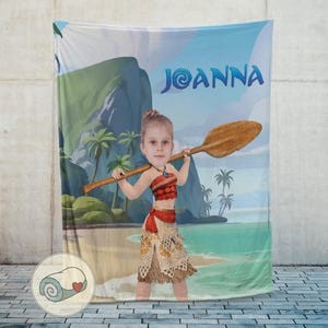 May include: A personalized blanket featuring a young girl dressed as a character from a movie, holding a wooden oar. The background depicts a tropical beach scene with palm trees, mountains, and the name "Joanna" in blue letters.