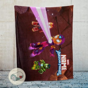 Op de afbeelding: Een bruine deken met een kleurrijke cartoonillustratie van vliegende figuren, waaronder een paars en geel figuur dat een roze straal uitzendt. De deken heeft de tekst "NAME" en "Awesome Friends" met het Marvel-logo.