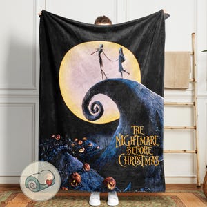 K&ouml;nnte beinhalten: Schwarze Fleece-Decke mit einer Szene aus "The Nightmare Before Christmas". Das Design zeigt Jack und Sally vor einem Vollmond, mit dem Filmtitel in Goldbuchstaben. Ein aufgerolltes Bild der Decke befindet sich in der Ecke.