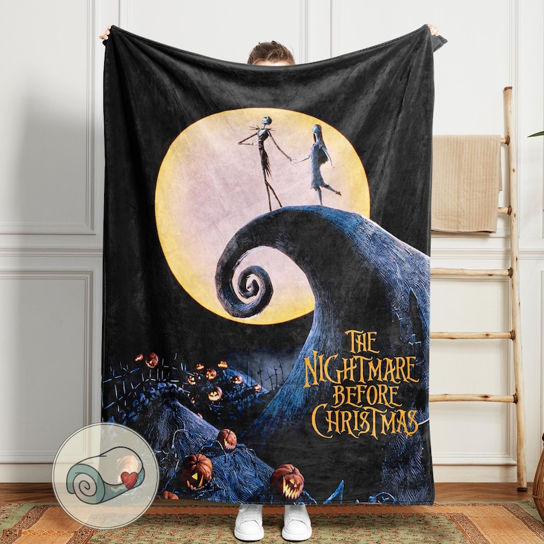 K&ouml;nnte beinhalten: Schwarze Fleece-Decke mit einer Szene aus "The Nightmare Before Christmas". Das Design zeigt Jack und Sally vor einem Vollmond, mit dem Filmtitel in Goldbuchstaben. Ein aufgerolltes Bild der Decke befindet sich in der Ecke.