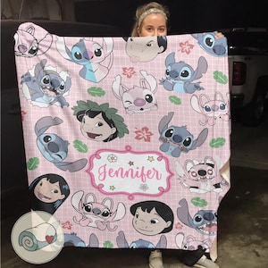 May include: Pink blanket featuring various cartoon character illustrations, including Stitch and Lilo. The blanket has a grid pattern and a decorative frame with the name "Jennifer".