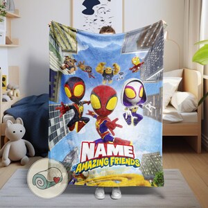 May include: A blue blanket featuring cartoon characters, including Spider-Man, with the text "NAME of AMAZING FRIENDS." The blanket has a cityscape background and is held up by a person. The blanket is made of a soft material.