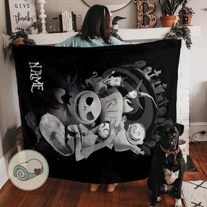 May include: Black blanket featuring a grayscale illustration of characters from "The Nightmare Before Christmas." The design includes Jack Skellington, Sally, and other figures, with the word "NAME" in white. A rolled-up blanket graphic is in the corner.