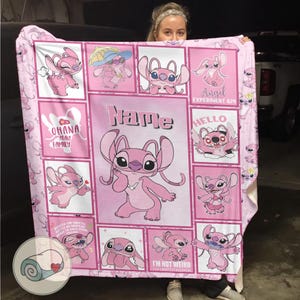 May include: Pink fleece blanket featuring the character Angel from Lilo & Stitch. The blanket has a grid design with various images of Angel, the text "Ohana Means Family", and the word "Name". The blanket is a soft, cozy item.
