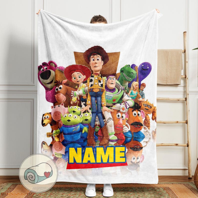 May include: White blanket with a vibrant graphic of Toy Story characters, including Woody and Buzz Lightyear. The blanket showcases a collection of characters from the film. The word "NAME" is printed in yellow on a red and blue banner.