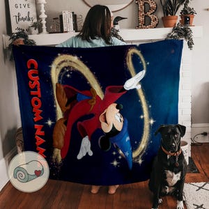 Op de afbeelding: Een marineblauwe deken met een kleurrijke illustratie van Mickey Mouse in een tovenaarsoutfit, met de tekst "CUSTOM NAME" in het rood. Het ontwerp bevat gouden wervelingen en sterren tegen een donkerblauwe achtergrond.