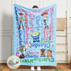 May include: A light blue blanket featuring cartoon characters and the name "Charlie" in various fonts and colors. The blanket showcases characters like Woody, Buzz Lightyear, and others from the Toy Story franchise, creating a playful and personalized design.