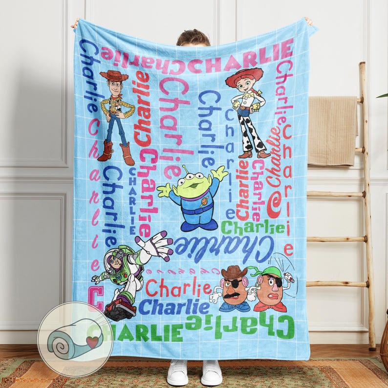 May include: A light blue blanket featuring cartoon characters and the name "Charlie" in various fonts and colors. The blanket showcases characters like Woody, Buzz Lightyear, and others from the Toy Story franchise, creating a playful and personalized design.