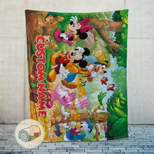 May include: A colorful blanket featuring Mickey Mouse, Minnie Mouse, Donald Duck, Daisy Duck, Goofy, and Pluto in a forest scene. The blanket has the text "CUSTOM NAME" in red. The blanket is rolled up in a small circle with a heart.