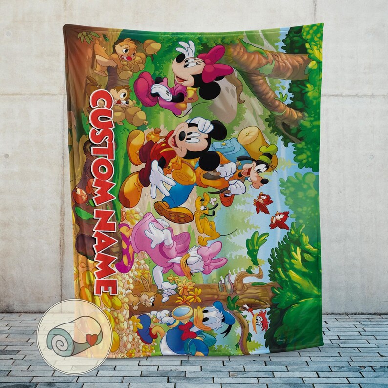 May include: A colorful blanket featuring Mickey Mouse, Minnie Mouse, Donald Duck, Daisy Duck, Goofy, and Pluto in a forest scene. The blanket has the text "CUSTOM NAME" in red. The blanket is rolled up in a small circle with a heart.