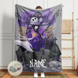 May include: A gray fleece blanket featuring a graphic of Jack Skellington from The Nightmare Before Christmas. The design includes a graveyard scene with purple and black accents, and the word "NAME" in white script.