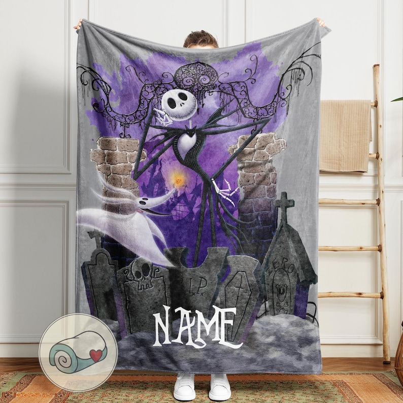 May include: A gray fleece blanket featuring a graphic of Jack Skellington from The Nightmare Before Christmas. The design includes a graveyard scene with purple and black accents, and the word "NAME" in white script.