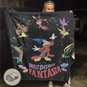 May include: Black blanket with Disney's Fantasia characters. Mickey Mouse as the Sorcerer's Apprentice is featured, alongside other characters and the film's title in a colourful, stylised font. A cosy home decor item, perfect for snuggling up with.