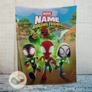 Pode incluir: Um cobertor com tema Marvel com o texto "NAME" e "Amazing Friends" e personagens de desenhos animados. O cobertor apresenta o Homem-Aranha, a Spider-Gwen e o Miles Morales em um fundo de c&eacute;u azul, &aacute;rvores verdes e uma ponte.