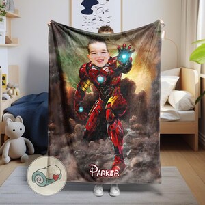 May include: A personalized blanket featuring a child's face superimposed on an Iron Man illustration. The blanket is predominantly red and gold, with a name, "Parker," printed at the bottom. The background has a cloudy, smoky effect.