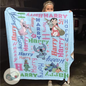 K&ouml;nnte beinhalten: Hellblaue Decke mit Zeichentrickfiguren und dem Namen "Harry" in verschiedenen Schriftarten und Farben. Die Decke hat ein Gittermuster und Illustrationen von Stitch und Lilo & Stitch-Charakteren. Eine aufgerollte Decke ist in der Ecke abgebildet.