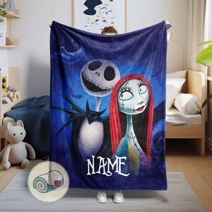 May include: A dark blue blanket featuring Jack Skellington and Sally from The Nightmare Before Christmas. The blanket has a personalized name in white script at the bottom. The characters are set against a dark blue background with a moon and bats.