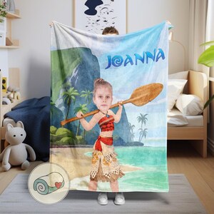 May include: A personalized blanket featuring a cartoon illustration of a person holding a wooden oar on a beach. The blanket has the name "Joanna" in blue letters. The design includes palm trees, a mountain, and a tropical beach scene. The blanket is light blue, green, and tan.
