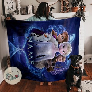 Pu&ograve; includere: Una coperta blu con i personaggi del film Frozen, tra cui Elsa, Anna, Olaf e Kristoff. La coperta ha uno sfondo blu scuro con un design a forma di cuore e la parola "NAME" in lettere bianche.