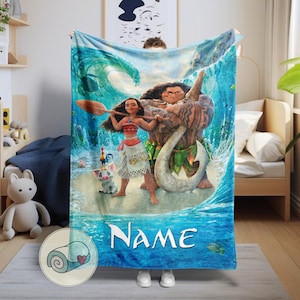 May include: A blue blanket featuring characters from the animated movie Moana. The blanket depicts Moana, Maui, Pua, and Hei Hei in front of a wave. The word "Name" is written in white across the bottom. The blanket is made of a soft material.