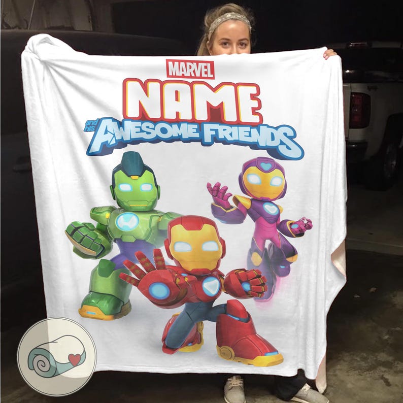 Op de afbeelding: Witte Marvel-deken met de tekst "NAME and Awesome Friends" en cartoon illustraties van Iron Man, Hulk en een ander personage. De deken heeft een opgerold beeld in de linker benedenhoek.