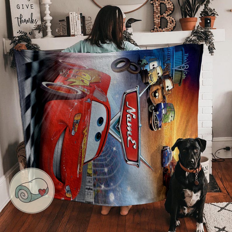 May include: A large, rectangular blanket featuring Lightning McQueen from the Cars movie. The blanket has a vibrant design with a red race car, the word "Name" in a stylized font, and other characters from the movie. The background includes a checkered flag and a sunset.