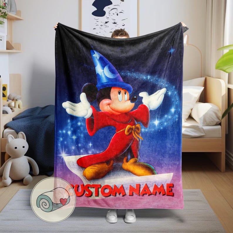 Pu&ograve; includere: Una morbida coperta con Topolino in abito da mago, con cappello blu e veste rossa, ambientata in un cielo stellato. La coperta ha la scritta "CUSTOM NAME" in rosso. Un plaid arrotolato con un cuore &egrave; nell'angolo.