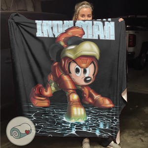 May include: Black blanket featuring a cartoon Mickey Mouse in an Iron Man suit. The blanket has the words "IRON MAN" in light blue block letters at the top. The background has a black and white lightning design.