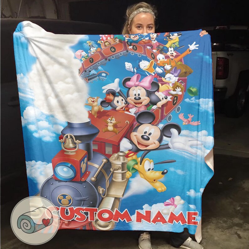 May include: A blue blanket featuring a colorful illustration of Mickey Mouse, Minnie Mouse, Donald Duck, and other Disney characters on a train and in the sky. The blanket has the text "CUSTOM NAME" at the bottom.