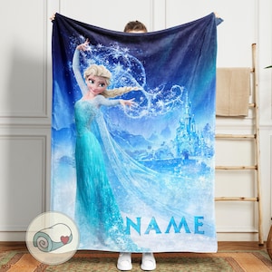 Op de afbeelding: Een blauwe deken met een prinses in een turquoise jurk en een kasteel op de achtergrond. De deken heeft het woord "NAME" in het blauw en een opgerolde deken met een hart in de hoek.