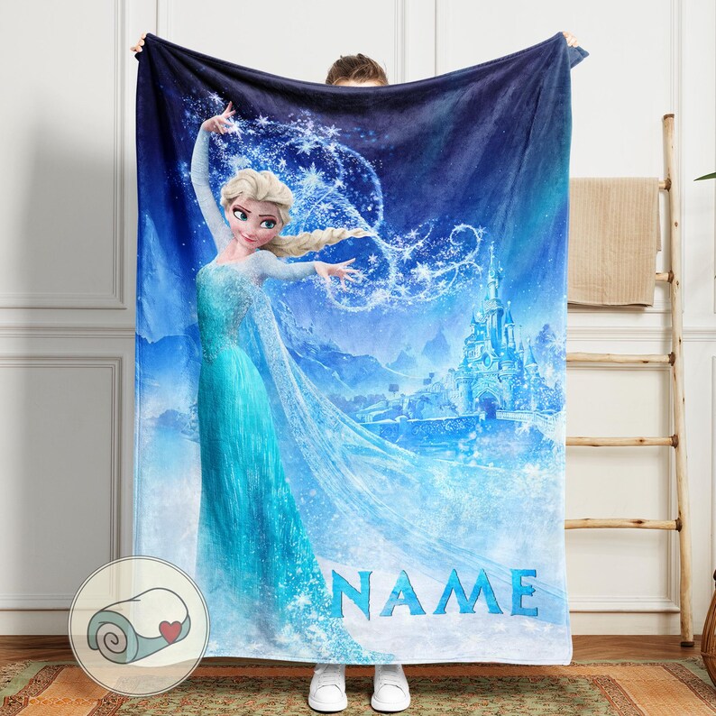 Op de afbeelding: Een blauwe deken met een prinses in een turquoise jurk en een kasteel op de achtergrond. De deken heeft het woord "NAME" in het blauw en een opgerolde deken met een hart in de hoek.