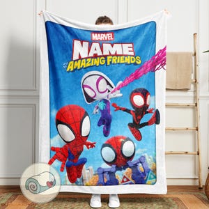 May include: A white blanket featuring a vibrant illustration of Spider-Man and his Amazing Friends. The blanket has a blue background with the Marvel logo and the text "NAME and his AMAZING FRIENDS". The characters are in action poses.