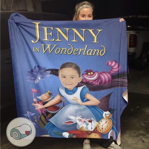 May include: A blue blanket featuring the text "JENNY in Wonderland" with an illustration of Alice in Wonderland characters. The blanket includes a portrait of a person as Alice, the Cheshire Cat, the White Rabbit, and the Queen of Hearts.