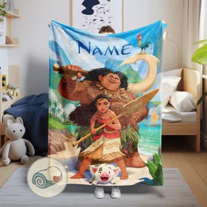 May include: A plush blanket featuring characters from the animated film Moana. The blanket has a blue sky background with the word "Name" in blue. The characters include Maui, Moana, Hei Hei, and Pua. The blanket is rolled up in a circular image.