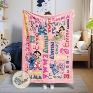 May include: A pink blanket featuring cartoon characters and the name "Emma" in various fonts and colors. The blanket has a grid pattern and includes images of characters from a popular animated movie.