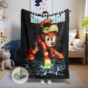 May include: Black blanket featuring a cartoon character in an Iron Man suit. The character is red and gold, with a yellow helmet. The blanket has the words "IRON MAN" in light blue across the top. The character is posed on a cracked, electric blue surface.