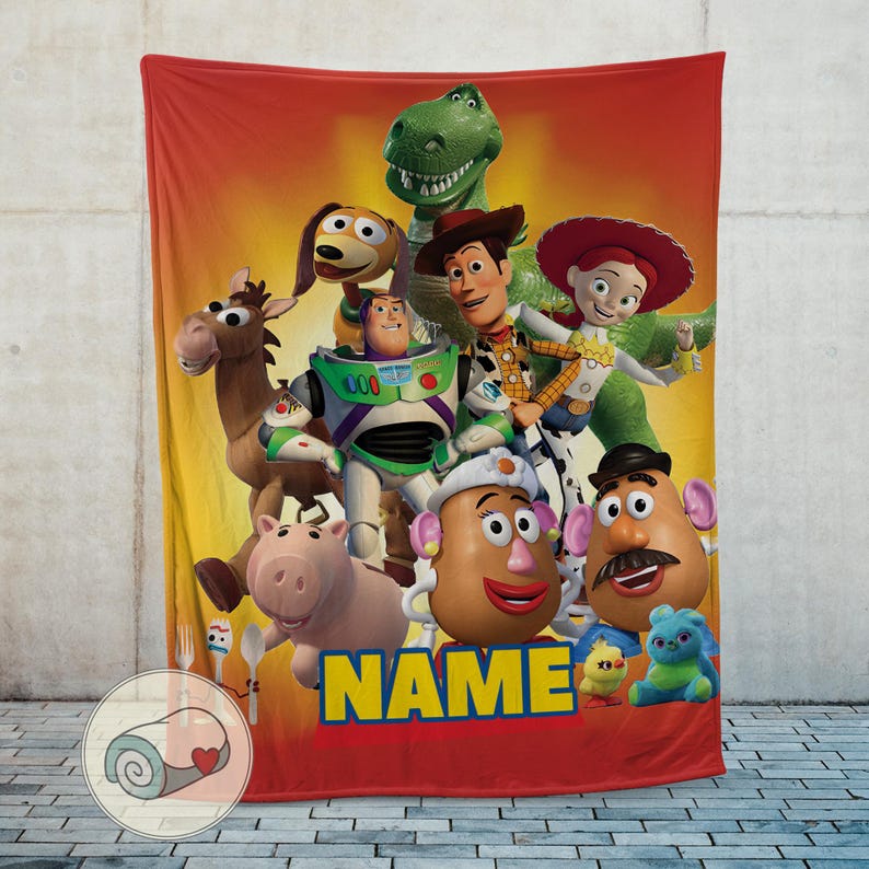 May include: A red and yellow blanket featuring a group of characters from the Toy Story movie franchise. The blanket has a red border and the word "NAME" in yellow letters.