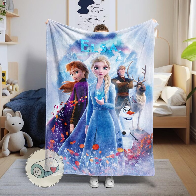 May include: A light blue blanket featuring characters from the movie "Frozen." The blanket displays Elsa, Anna, Kristoff, Sven, and Olaf against a snowy mountain backdrop. The word "ELSA" is written in blue at the top.