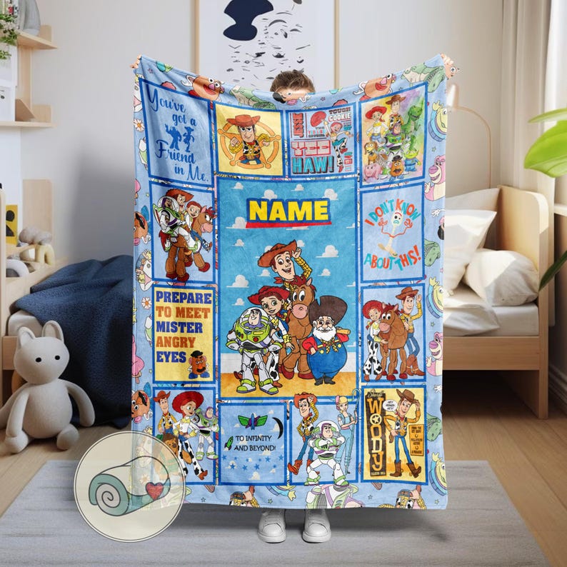 May include: A light blue blanket featuring characters from the animated film Toy Story. The blanket has a central panel with the word "NAME" and several character panels. Phrases like "You've got a friend in me" and "To infinity and beyond" are also visible.